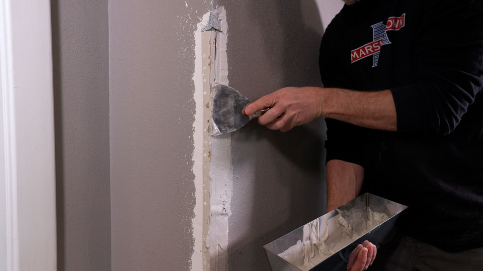 using a joint knife to apply mud to both sides of the corner